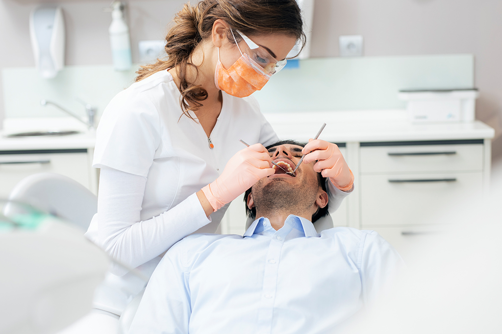Uma pessoa sorrindo abertamente, mostrando dentes brancos e saudáveis, com um dentista sorrindo ao fundo.