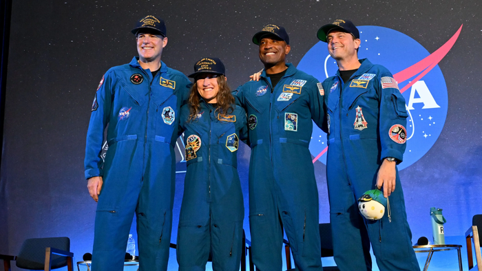 Imagem dos astronautas da Artemis II sorrindo após o retorno à Terra, com a espaçonave Orion ao fundo.