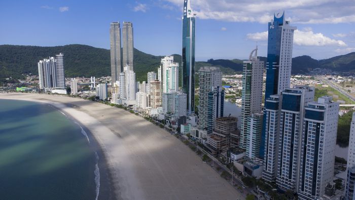 Visão de baixo para cima de prédios altos em uma cidade densa, com o céu parcialmente visível.